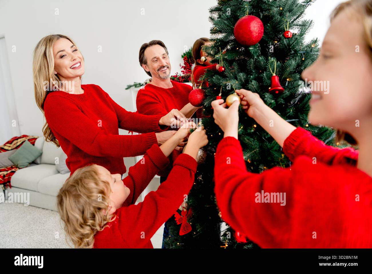 Die Familie versammelt sich, um zu Hause einen Weihnachtsbaum zu schmücken, und teilt Freude und Zweisamkeit in dieser Weihnachtszeit Stockfoto