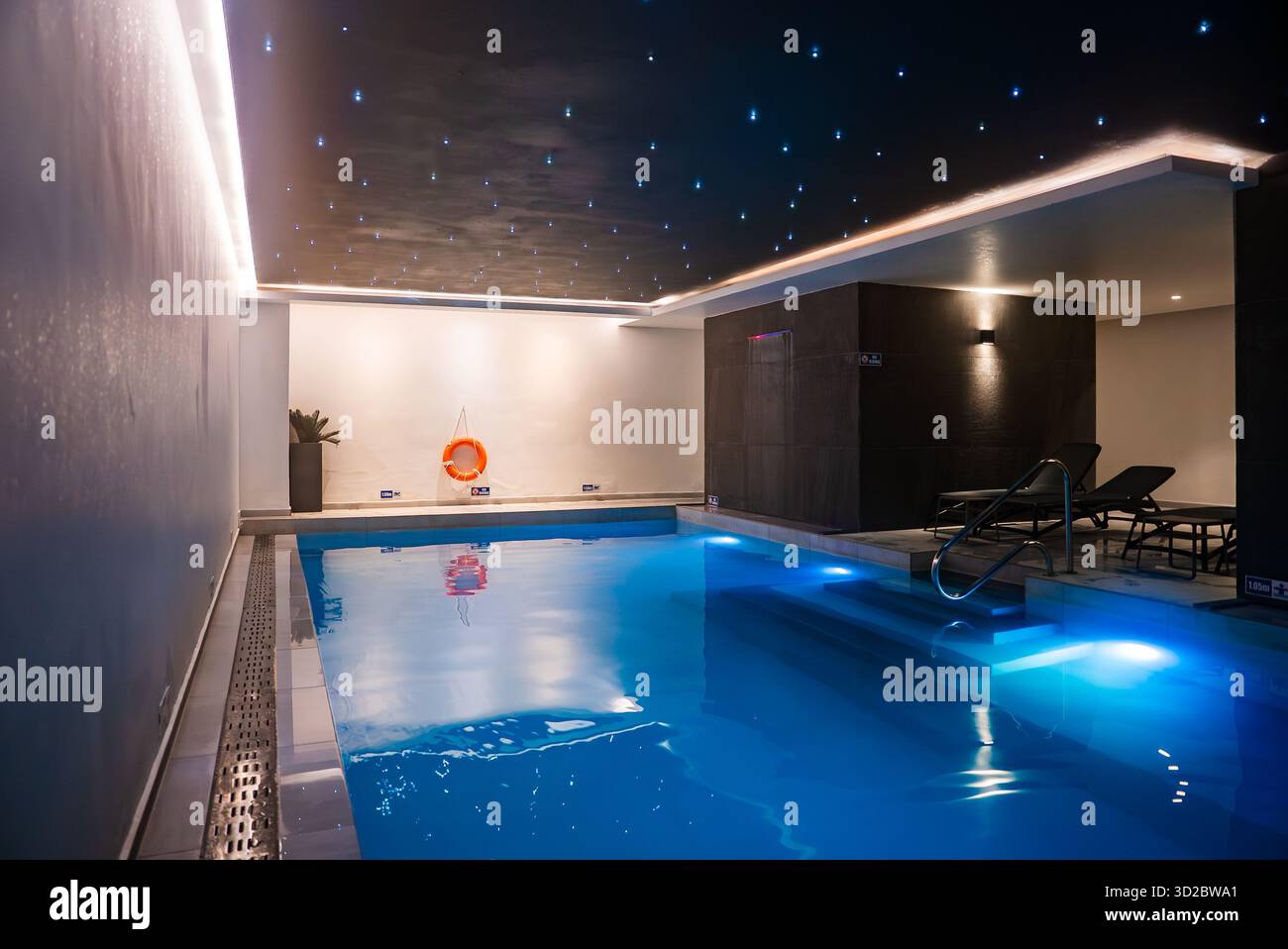 In einem Spa in Mellieha, Malta, erstrahlt ein Innenpool unter einer Decke mit Sterneneffekt. Lounge-Stühle, minimalistische Wände, sanfte Beleuchtung, Sicherheitsring und a n Stockfoto