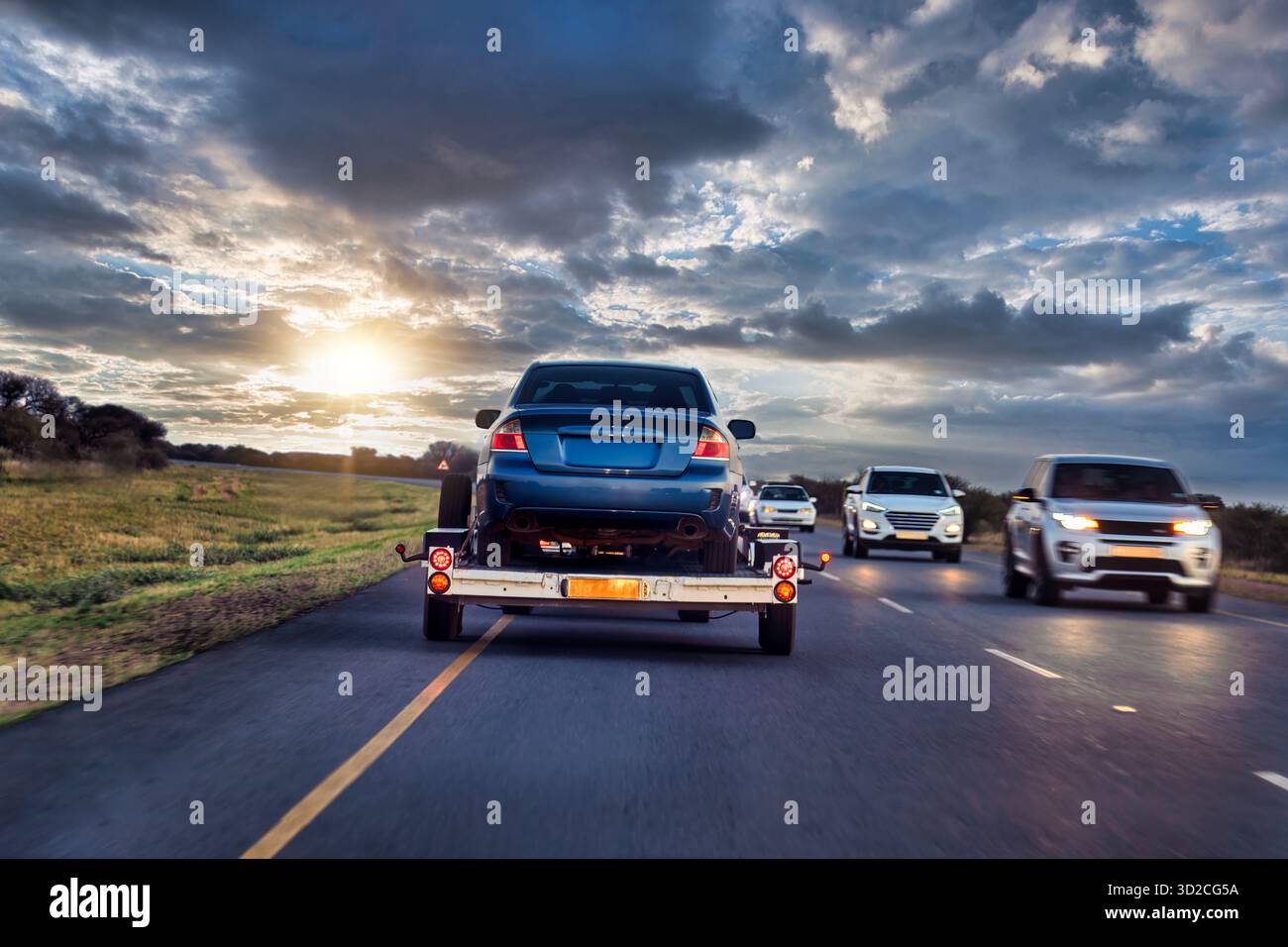 Auto mit niedrigem Anhänger auf der Straße, Auto-Fahrzeuge mit Träger Transporter Transporter Transporter Autobahn Transport Logistik Transport mit Fahrer, Afrika Sonnenuntergang Stockfoto