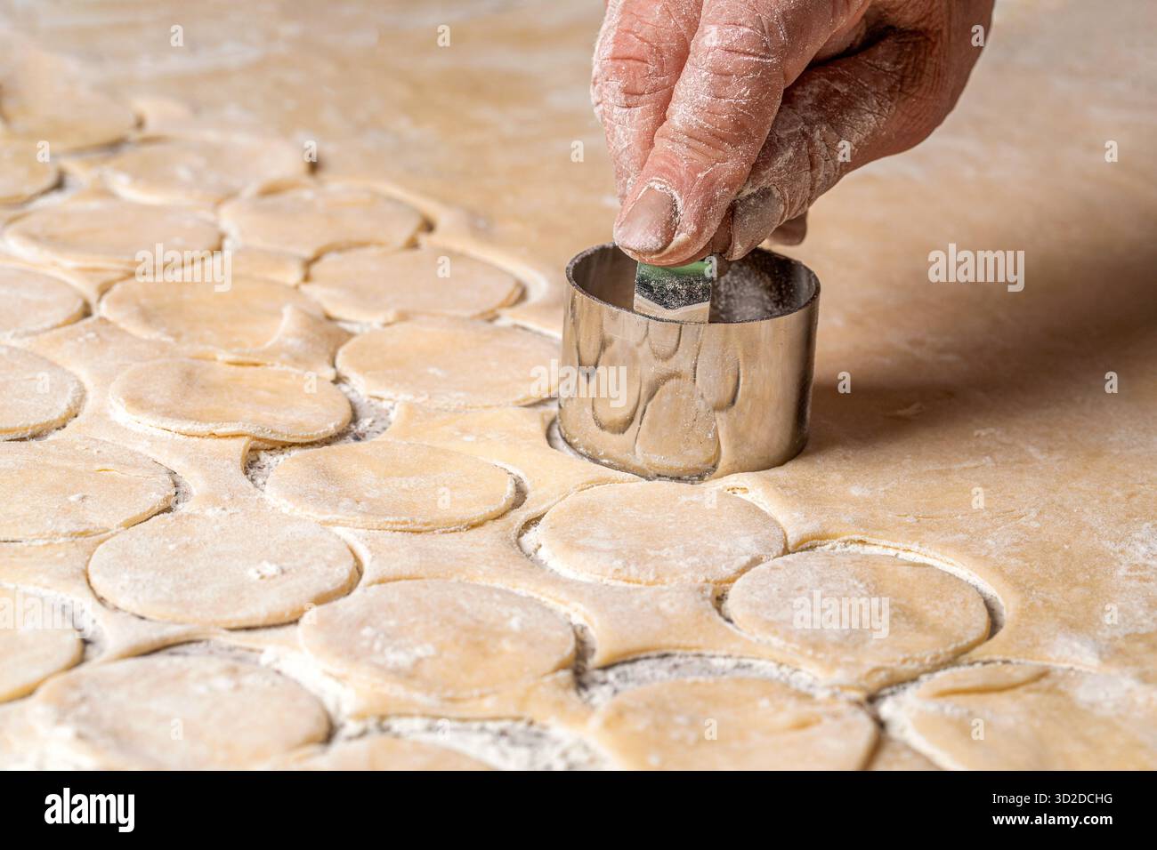Zubereitung des Teigs zum Backen, ein großes Stück des Teigs liegt auf dem Tisch und der Koch schneidet kleine Kreise mit eiserner Form aus. Stockfoto
