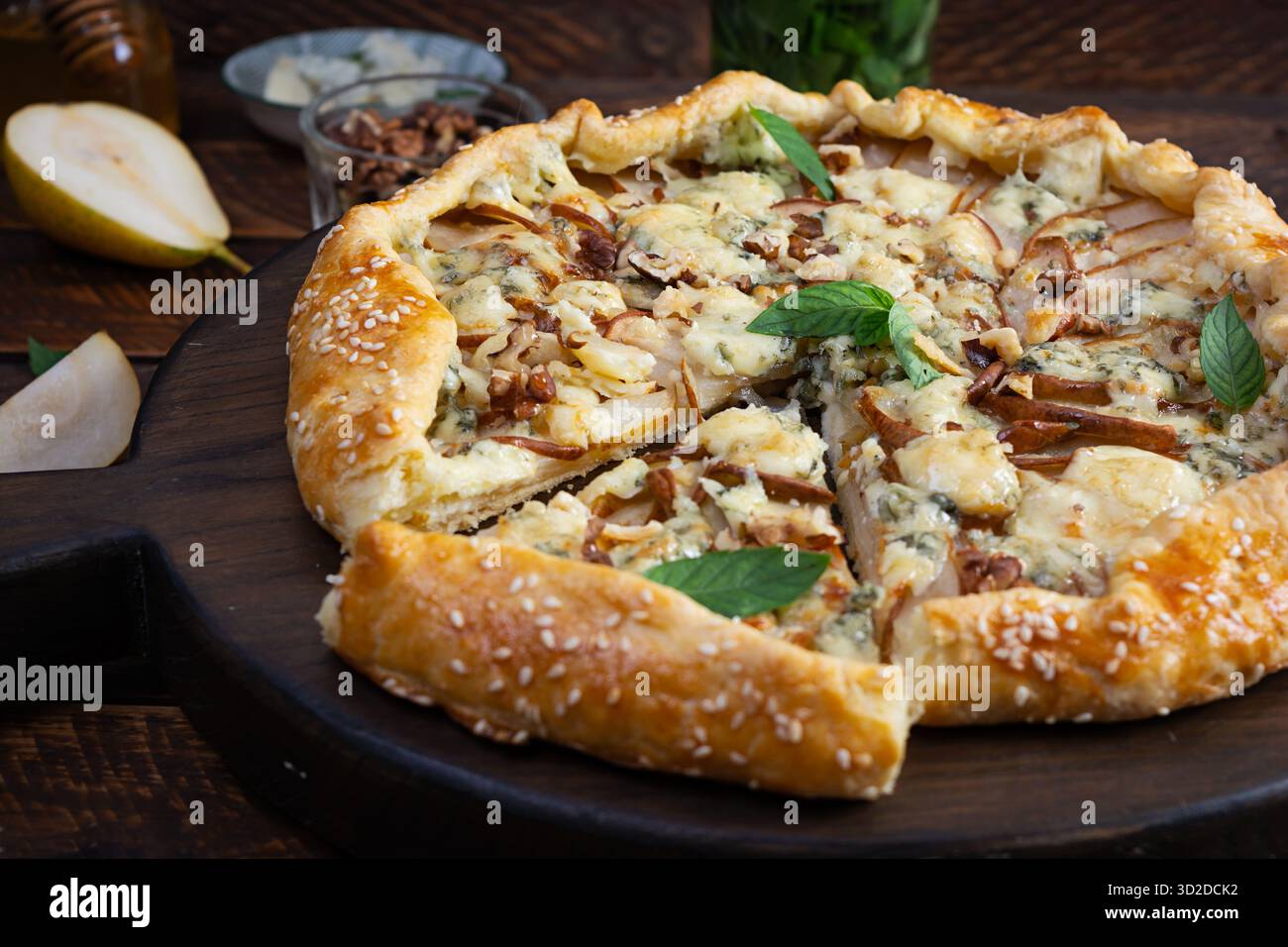 Hausgemachte Birnenbrie Galette auf Holzbrett, goldene Kruste, geschmolzener Käse, Honigglasur. In Scheiben geschnittene Galette mit Birnen und Käse Stockfoto