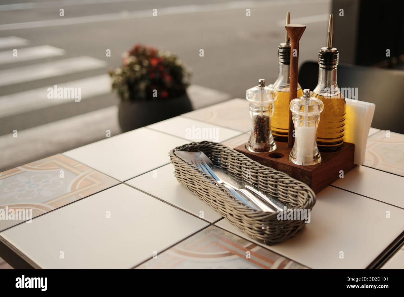 Ordentlich angeordneter Esstisch mit Olivenölflaschen, Gewürzen und Metallbesteck im Korb. Stockfoto