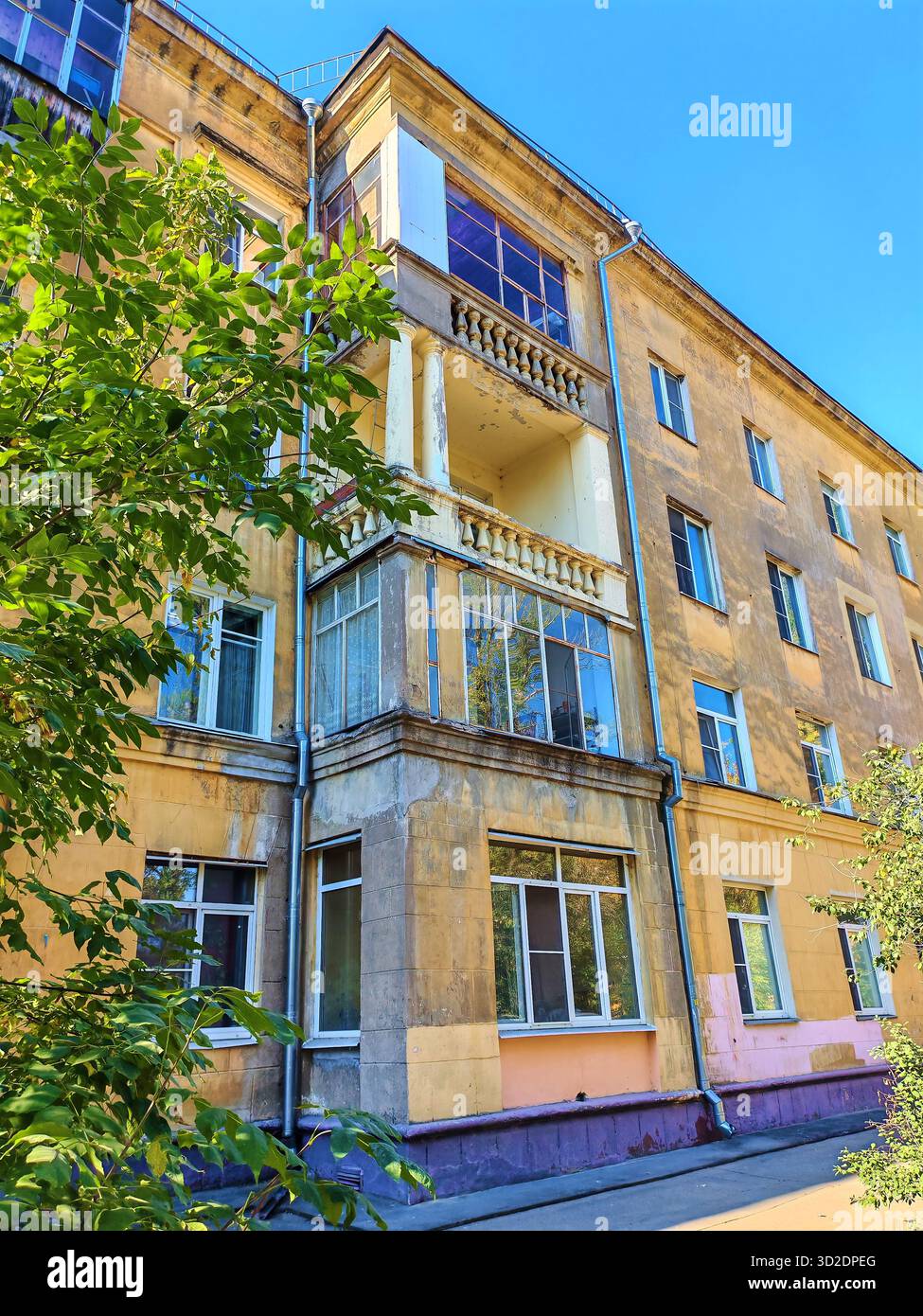 Altes gelbes Wohngebäude mit abgenutzten Balkonen und dekorativen Säulen, die Anzeichen von Putzschäden und Witterungseinflüssen zeigen. Das Foto hebt die Fassade hervor Stockfoto
