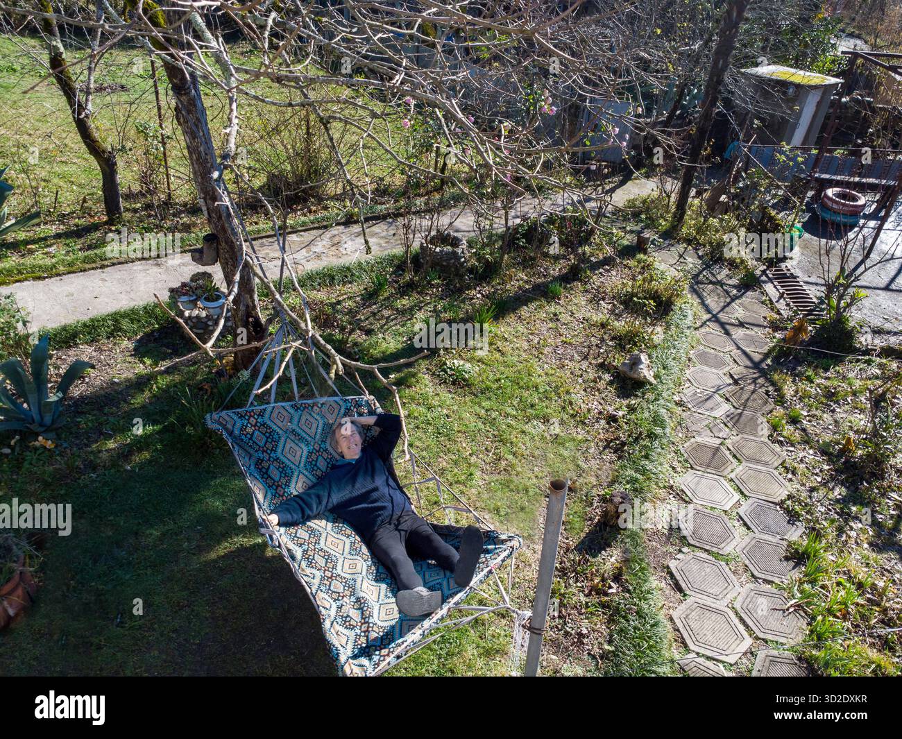 Glücklicher chinesischer Mann in seinen 60ern, der während der Wintermonate in Florida in einer Hängematte (im Hinterhof des Hauses) die Sonne genießt Stockfoto