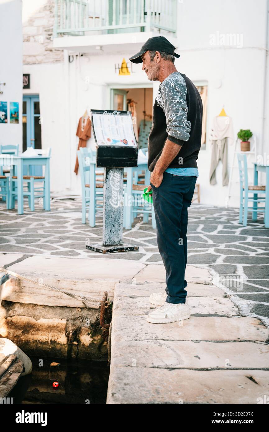 Ein Mann fischt mit einer Schnur von der Kaimauer im alten Hafen von Naoussa, Paros, Griechenland Stockfoto