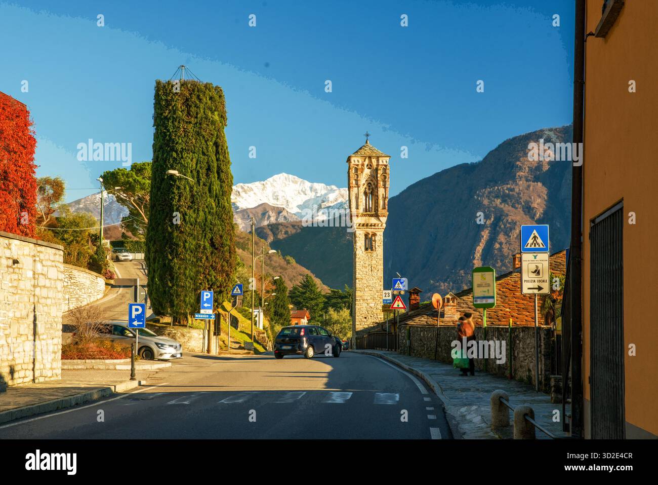 Asphaltstraße entlang der Küste von Como nach Norden und hoher Glockenturm der katholischen Kirche. Leute, die UNS wehkelten, wandern auch mit chinesischer Ethnizität Stockfoto
