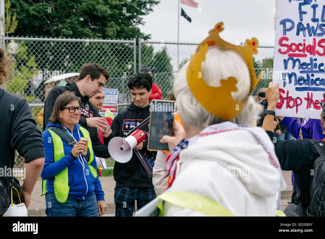 Die reife Demonstrantin in Papierkrone zeichnet junge Trump-Gegenprotestierende auf ihrem Handy auf der Demonstration „No Kings“ in St. Paul, USA, 14. Juni 2025 Stockfoto
