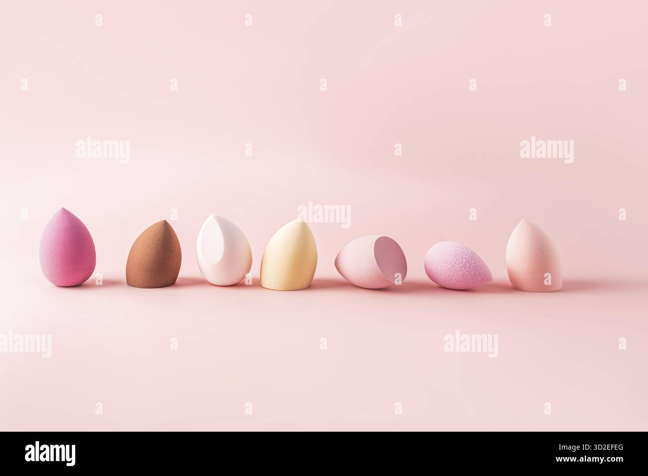 Kosmetik-Kosmetik-Schwamm, der in verschiedenen Farben in rosa Farbtönen angeordnet ist. Rosafarbener Hintergrund. Vorderansicht. Anwendungswerkzeug für flüssige Kosmetik Stockfoto