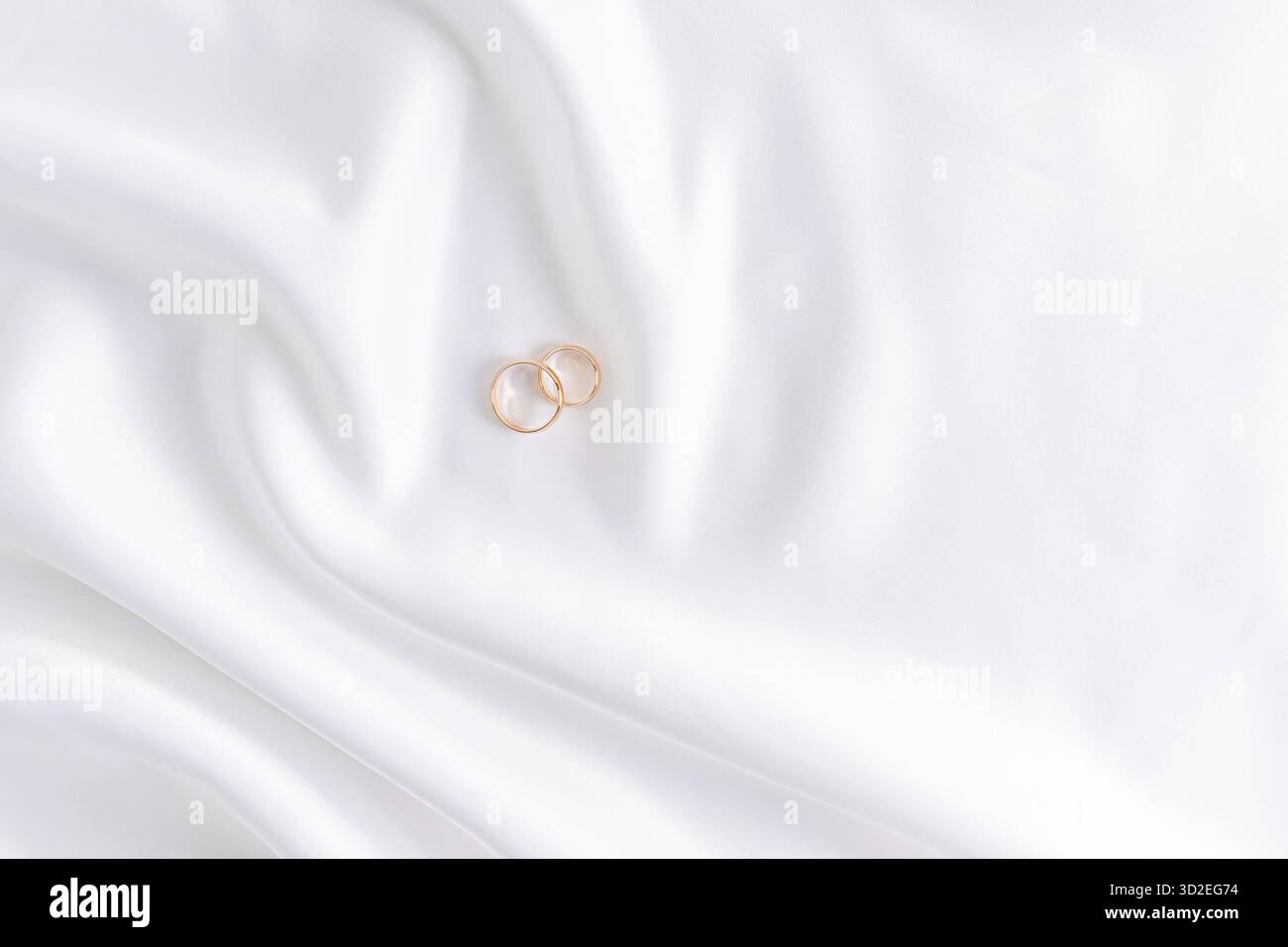 Festlicher Hochzeitshintergrund mit zwei goldenen Ringen auf weißem Satin-Material. Kopierbereich Stockfoto