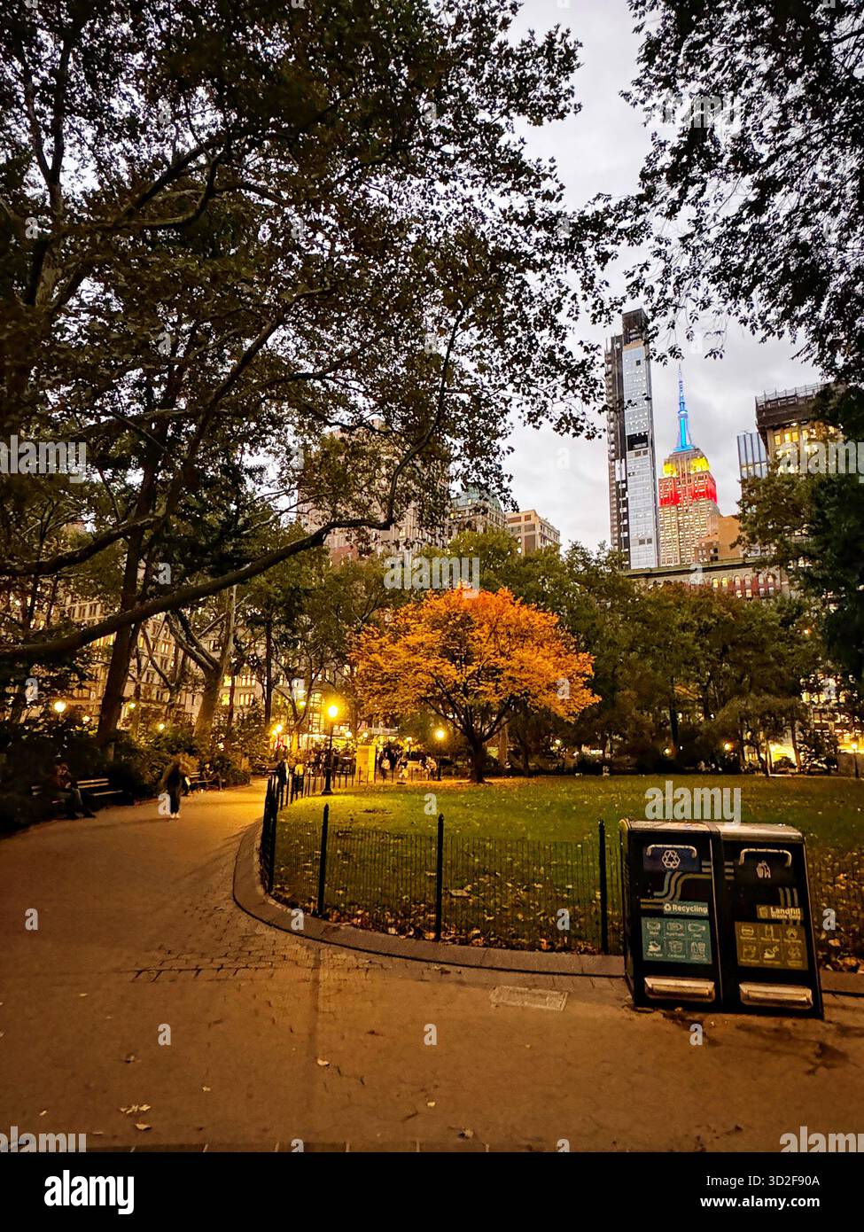 Herbstabend im Madison Square Park in der Nähe des Flatiron Building, NYC, mit farbenfrohen Blättern und dem Empire State Building in der Ferne. - Smartphone-aufgenommenes Stockfoto