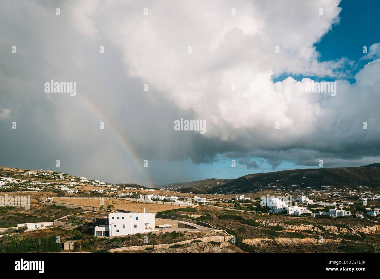 Blick von der Terrasse eines Ferienhauses auf eine Wolke mit lokaler Regendusche und einem Regenbogen über Parikia, Paros, Griechenland Stockfoto