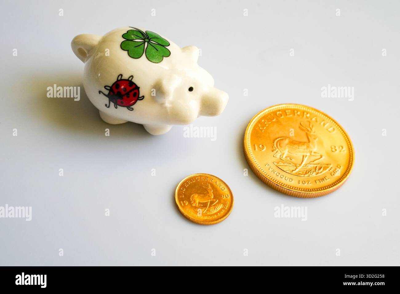 Schweinebank mit Einem Lucky Shamrock und Einem Marienkäfer, umgeben von glänzenden goldenen Krügerrand-Münzen, auf Einem Plain Grey Hintergrund, symbolisiert Thrift und Glück. Stockfoto