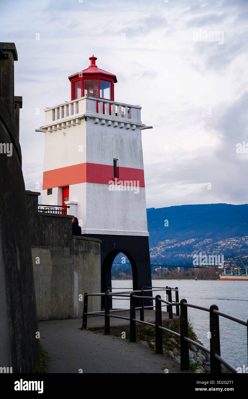 Seitenansicht des Brockton Point Lighthouse entlang der Ufermauer des Stanley Park mit Blick auf Burrard Inlet und die North Shore Mountains in der Ferne. Stockfoto