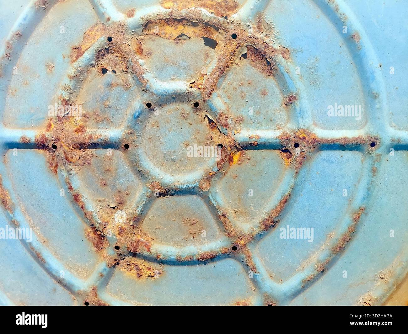 Der Boden eines blauen Metallgehäuses zeigt eine rostige, strukturierte Oberfläche mit dunklen Flecken und Löchern, was darauf hindeutet, dass sie den Elementen im Laufe der Zeit ausgesetzt ist. Stockfoto