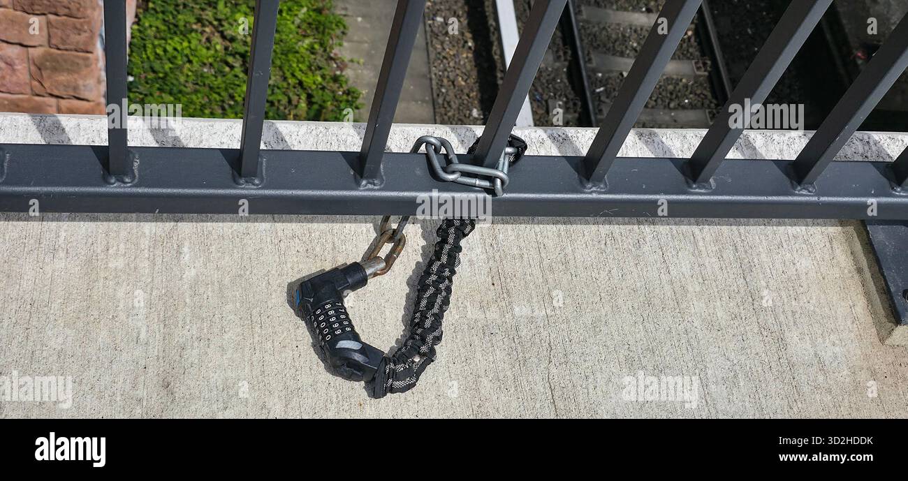 Berlin, Deutschland - 03. Juli 2025: . Das schwarze Kettenschloss sichert ein Metallgeländer in der Nähe von Bahngleisen in einer städtischen Umgebung - Smartphone-aufgenommenes Stockfoto