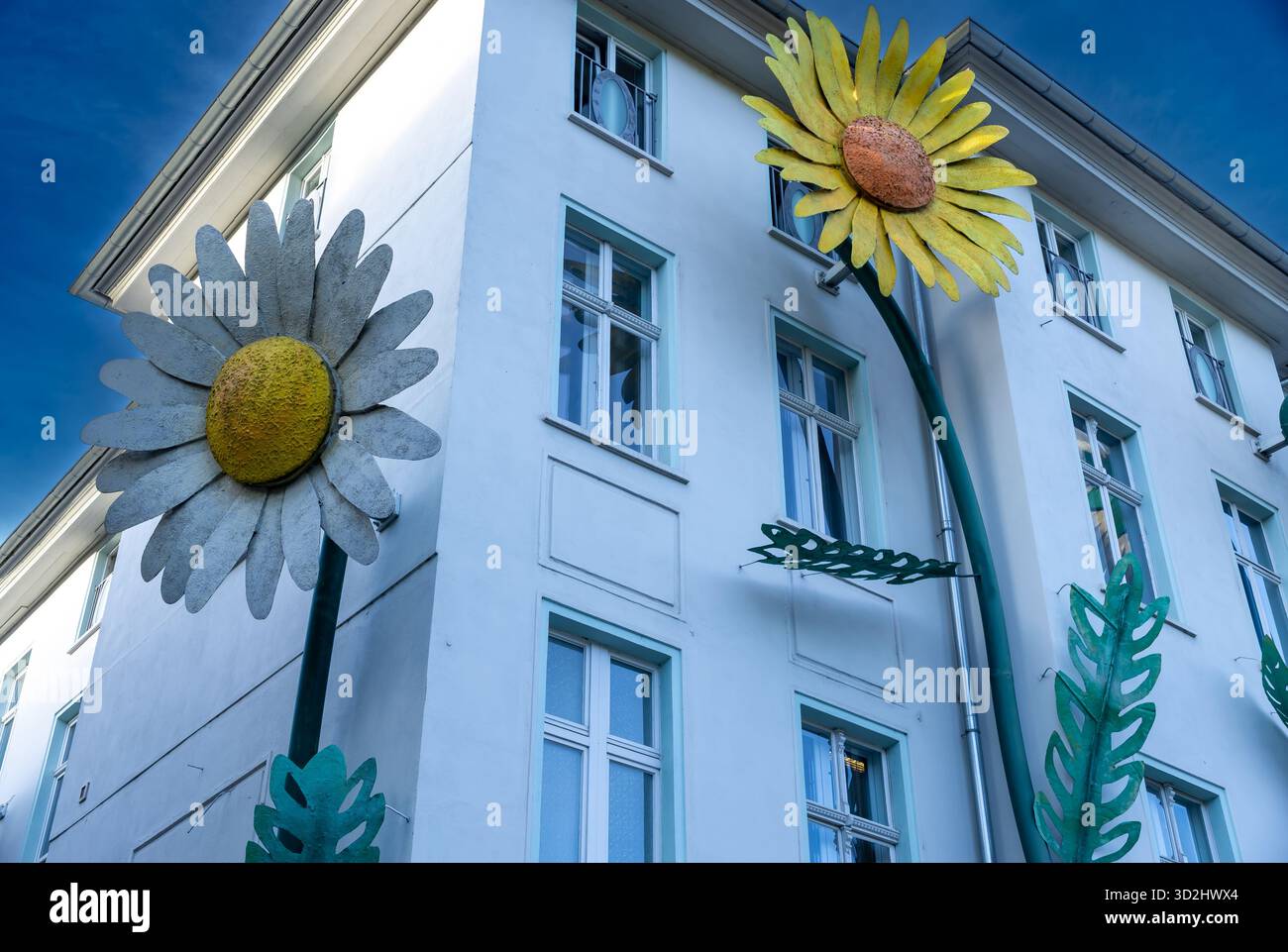 Eine Gebäudefassade in Berlin, Deutschland, mit riesigen Blumenskulpturen, darunter Gänseblümchen und Sonnenblumen, die mehrere Stockwerke hochklettern. Stockfoto