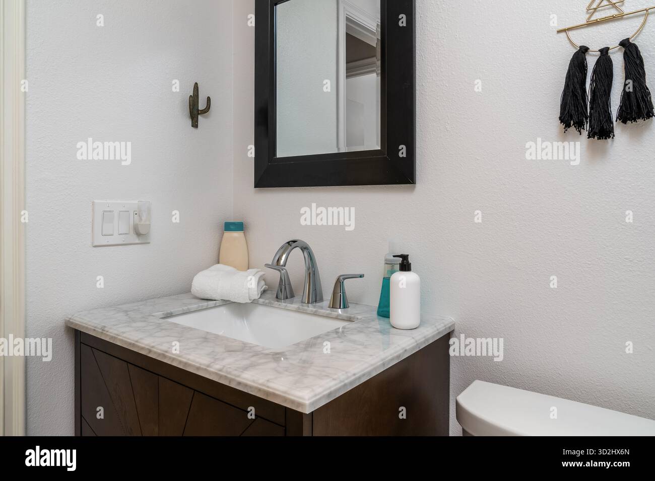 Weißes modernes Badezimmer mit Marmorwaschbecken, Wasserhahn, Spiegel, Handtuch, Seife, Lotion, Wandhaken Stockfoto