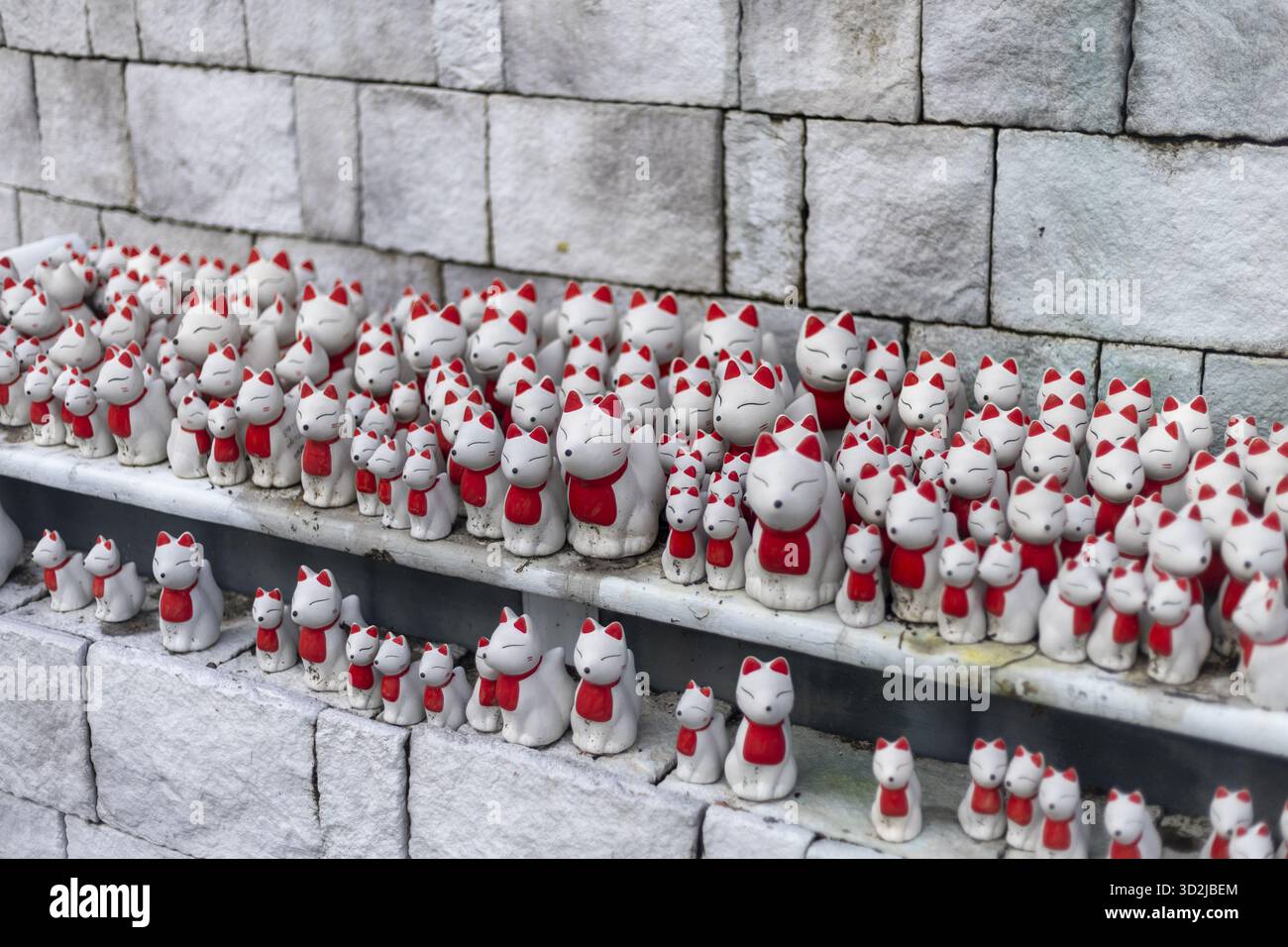 Bezaubernde Sammlung weißer Keramik-Glückskatzenfiguren mit Steinvorsprung, jede mit leuchtenden roten Akzenten verziert. Entzückendes orientalisches Reizsymbol Stockfoto