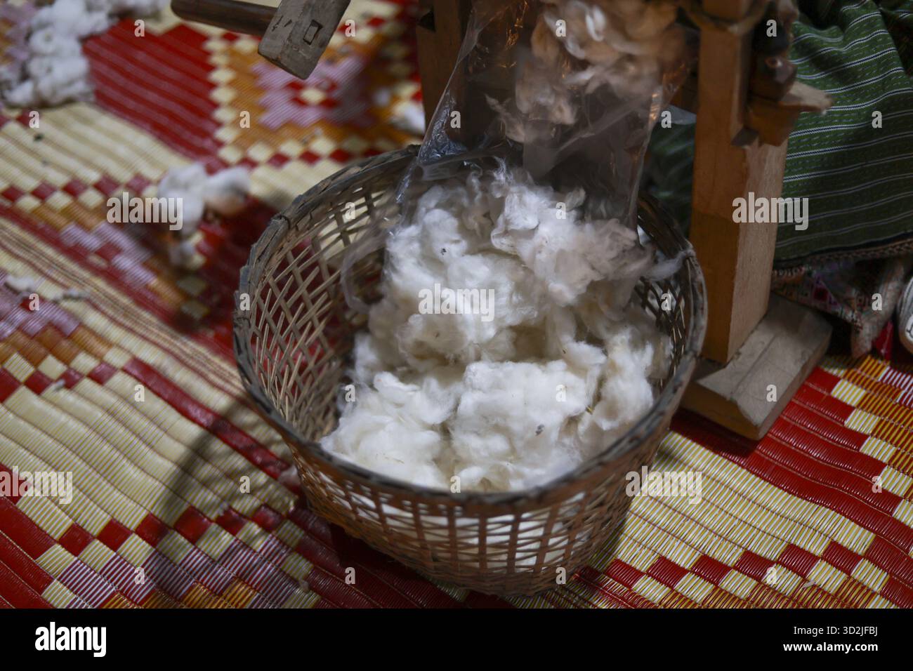 Rohe Baumwollfasern im Korb während des Entkörnungsmaschinenprozesses. Ruhiger, fokussierter Einblick in die Welt der traditionellen Textilherstellung und authentischer Handwerksprofis Stockfoto