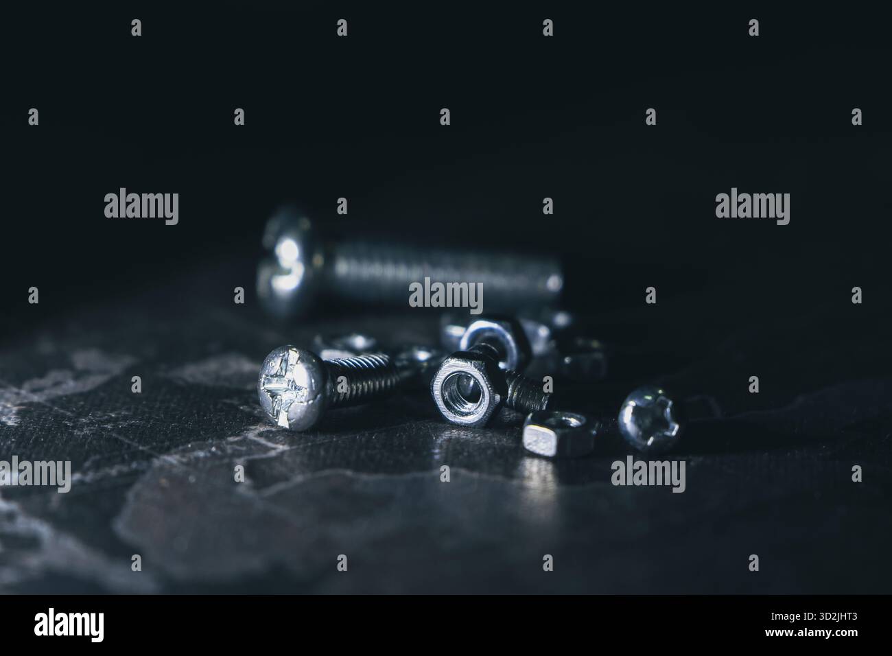Dramatische Makroaufnahme von Haufen von Metallmuttern und -Bolzen. Industrielle Stahlbauteile, einschließlich Schraube und Befestigungselement, auf dunkelschwarzem Hintergrund Stockfoto