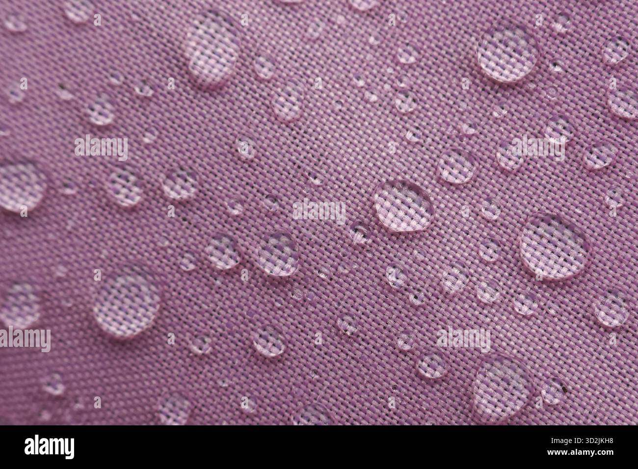 Glitzernde Wassertröpfchen sind mit anmutig violettem Gewebe verziert, was seine hervorragenden wasserfesten Eigenschaften unterstreicht. Strukturierte Oberfläche sorgt für fesselnde Momente Stockfoto