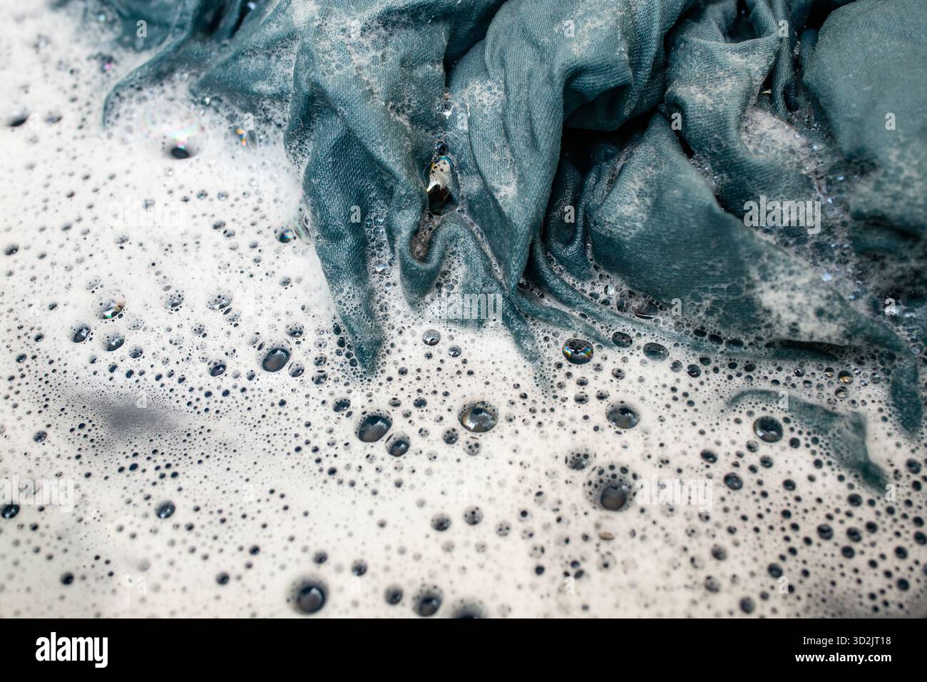 Ein blaues Gewebe auf heißem Wasser mit Reinigungsmittel einweichen, um Flecken besser zu entfernen, weicher Fokus Stockfoto