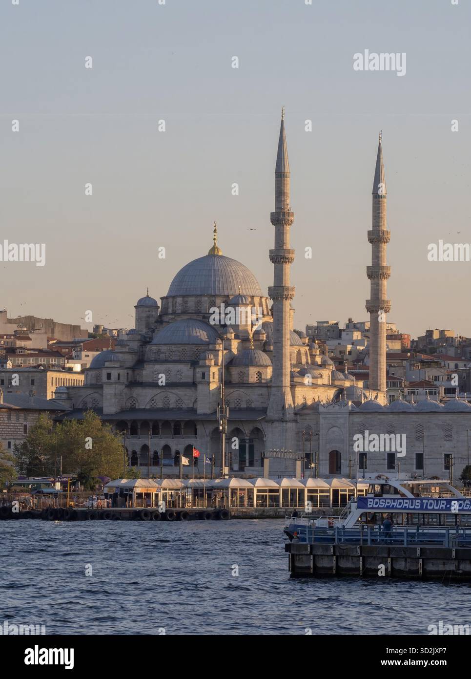 Blick auf die neue Moschee und die Fährschiffe auf dem Goldenen Horn in Istanbul, Türkei, mit Stadtgebäuden und Kuppeln, die von warmem Abendlicht beleuchtet werden Stockfoto