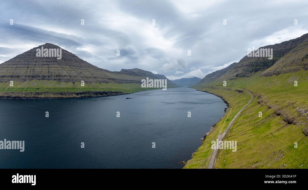 Abgeschiedener Fjord der Färöer und Berge am Meer mit einer Fischzucht und einem Hilfsschiff im Wasser Stockfoto