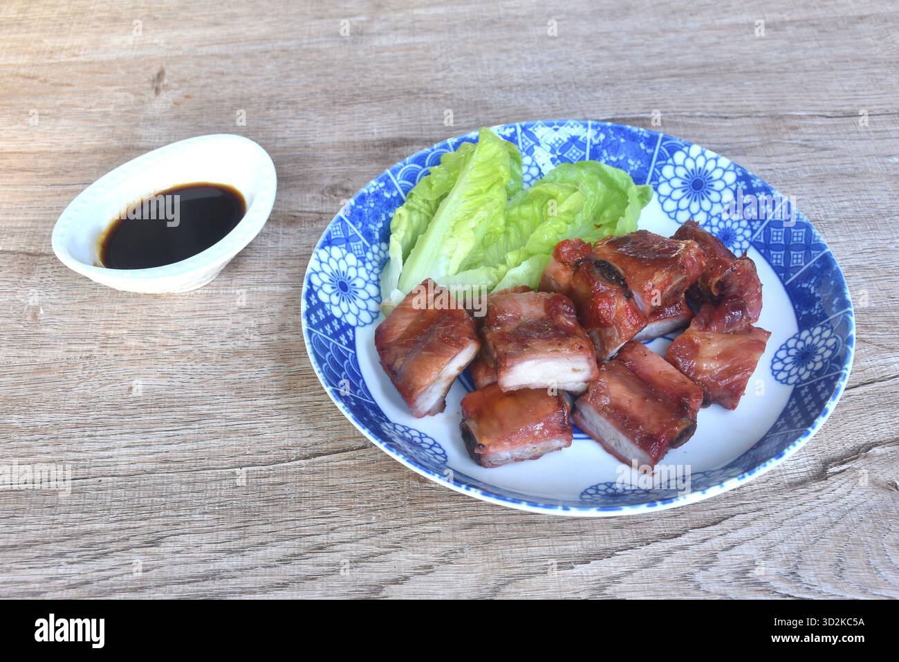 Gebratenes knuspriges Schweineknochen oder Rippchen mit Babysalat auf Teller, in einer Tasse mit schwarzer süßer Soße Stockfoto