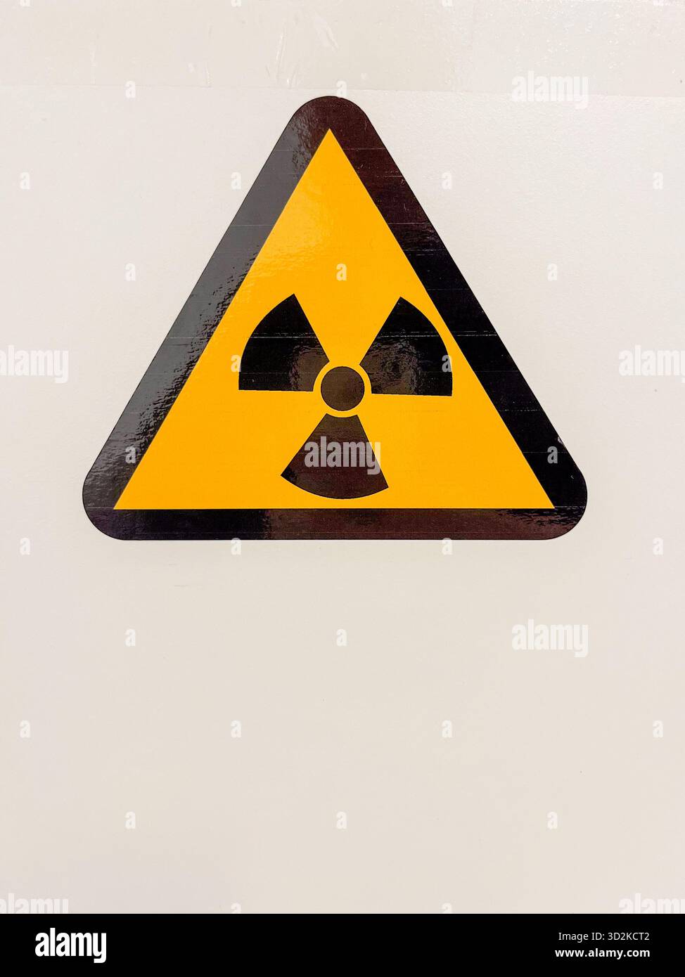 Dreieckiges Warnschild mit Strahlungssymbol, gut sichtbar an einer weißen Wand angebracht, das wichtige Sicherheitshinweise und Vorsicht in Gefahrenbereichen vermittelt Stockfoto