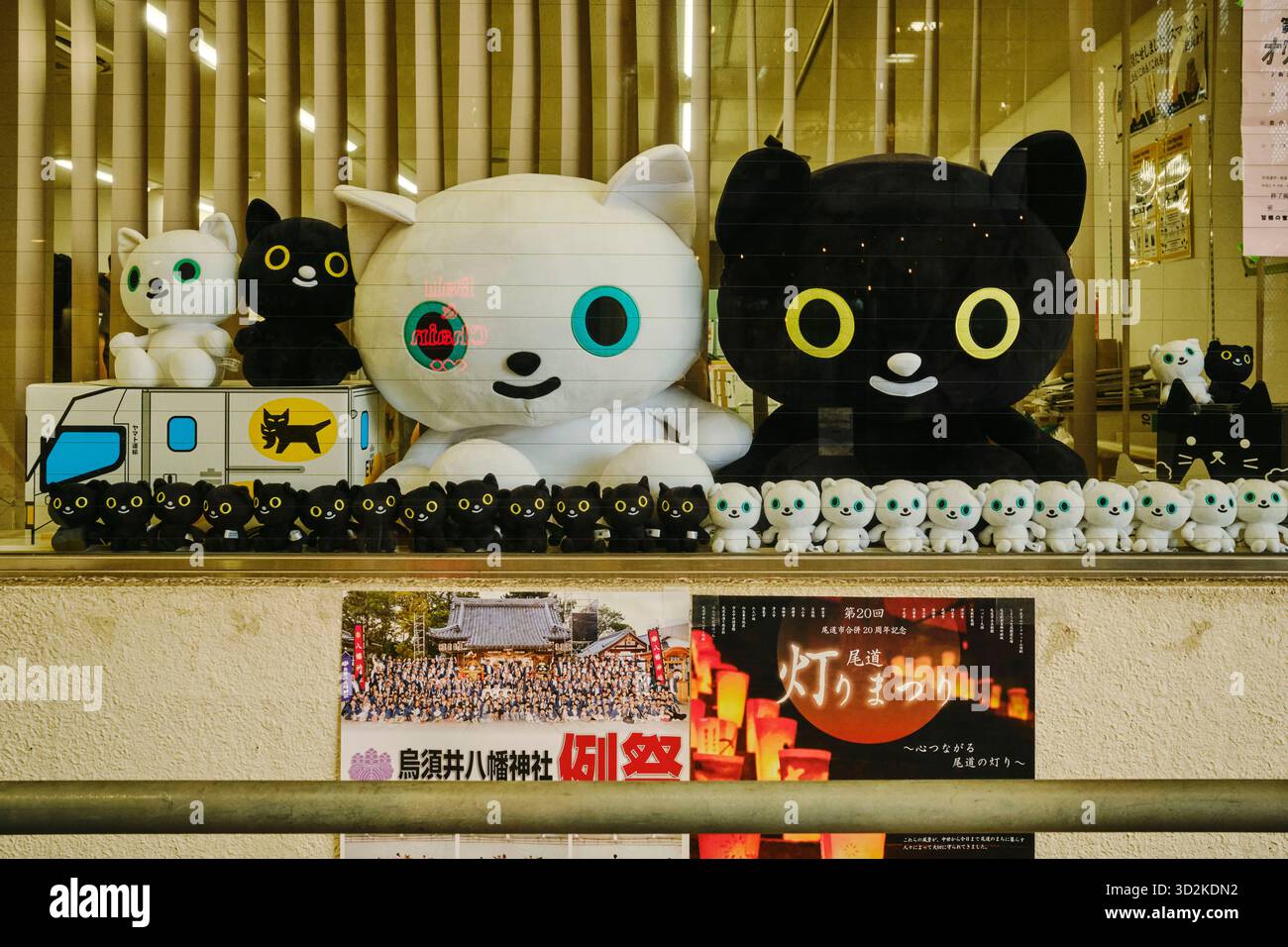Reihen von schwarz-weißen Katzenplushies in verschiedenen Größen, die im Glasladen des Yamato Transport Shops entlang der Einkaufsstraße Onomichi Hondori ausgestellt werden Stockfoto