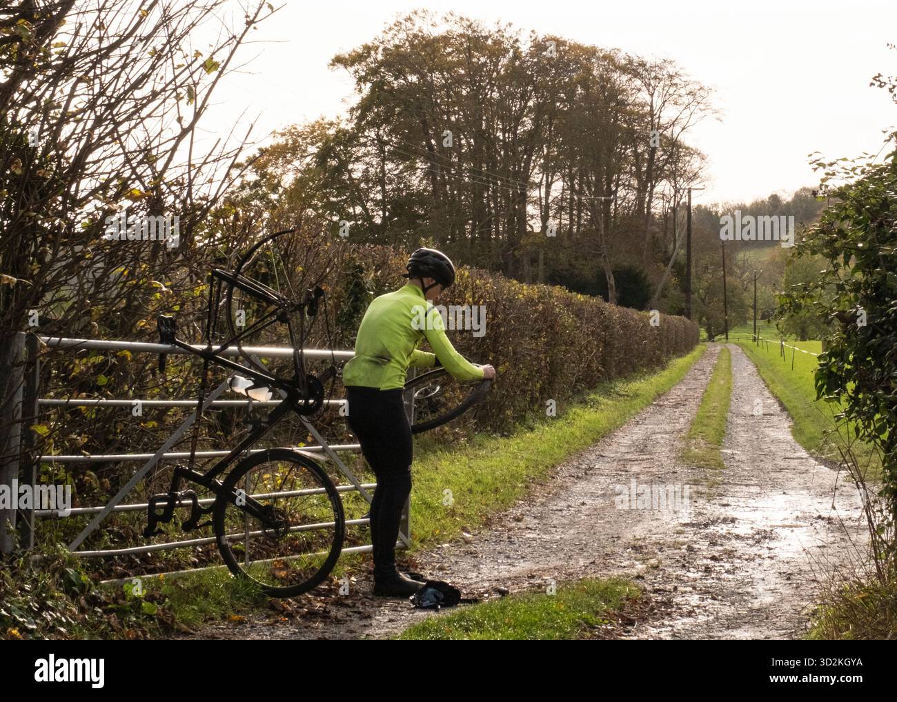 Ein Radfahrer, der auf den Füßen denkt, repariert einen Reifenschaden am Rande einer Landstraße Stockfoto