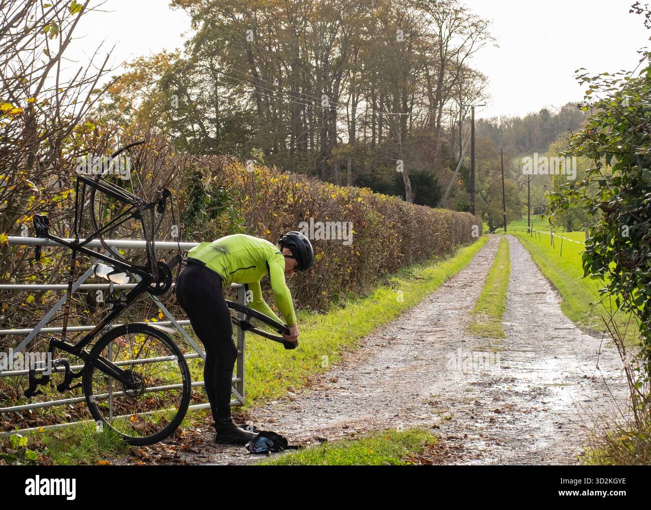 Ein Radfahrer, der auf den Füßen denkt, repariert einen Reifenschaden am Rande einer Landstraße Stockfoto