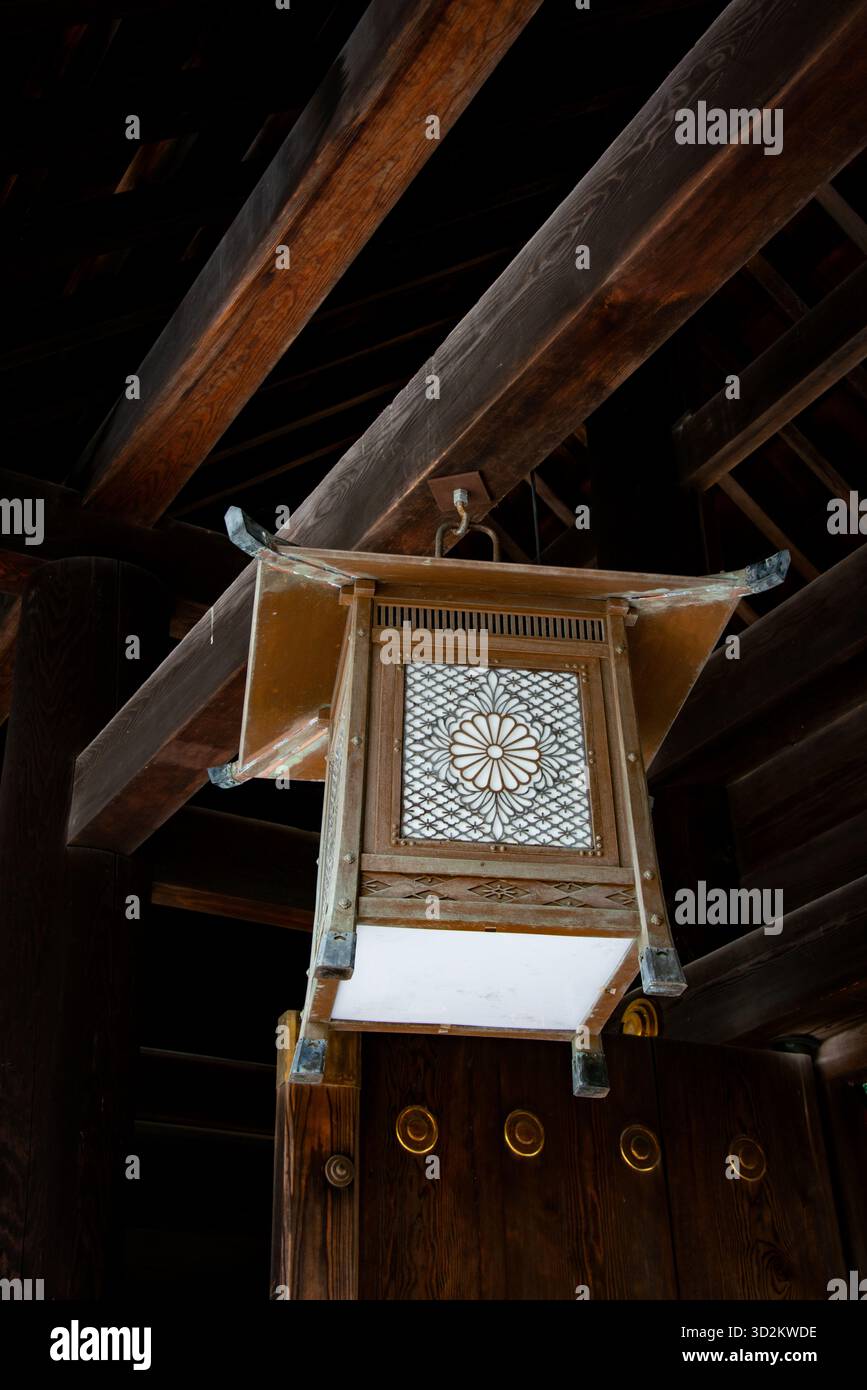Eine detaillierte Aufnahme einer alten, verzierten hölzernen Laterne, die an den dunklen Balken eines japanischen Tempels oder Schreins hängt Stockfoto