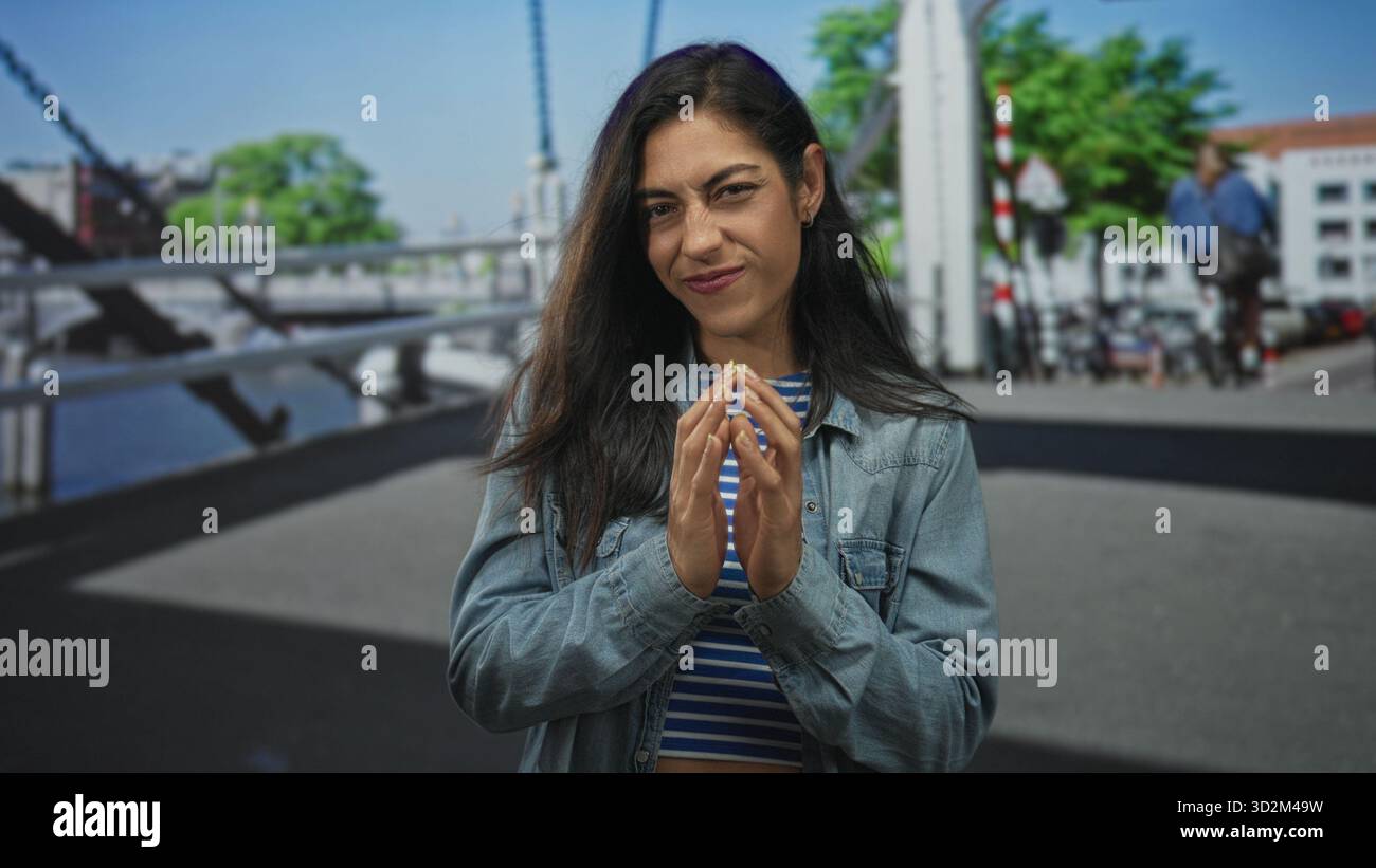 Frau mit den Fingern und sichtbaren Händen, mit Jeansjacke und gestreiftem Oberteil auf einer Straße am Kanal; ruhiges Selbstvertrauen. Stockfoto