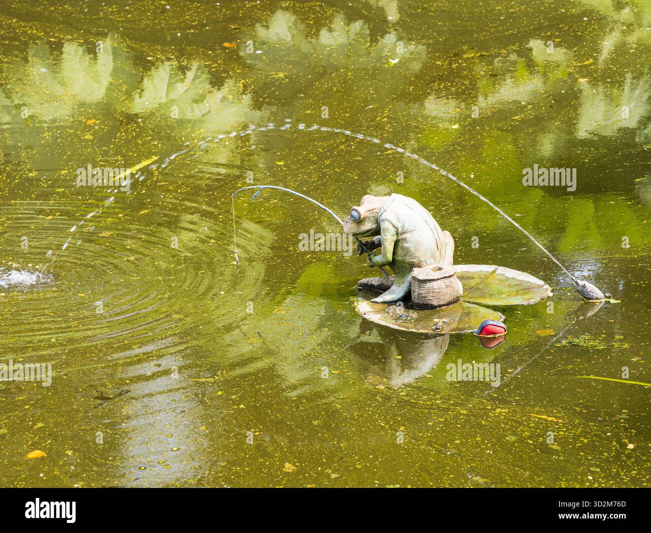 Gartenschmuck eines Fischfrosches auf einem Lilienpad unter einem bogenförmigen Wasserstrahl aus einem Fischmaul Stockfoto