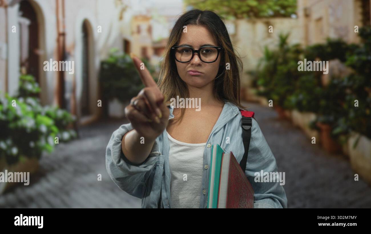 Frau zeigt den Finger in der Straße nach vorne, hält Notizbücher und Rucksack, während sie Brille und Jeansshirt trägt; Bestimmungsgrenze. Stockfoto