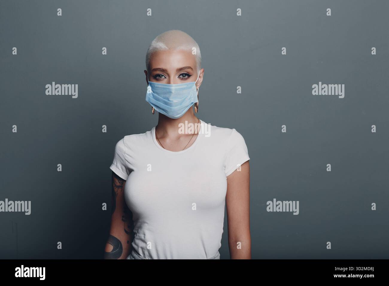 Millenial junge Frau in medizinischen Schutz Gesichtsmaske mit kurzen blonden Haaren Porträt stehend innen Stockfoto
