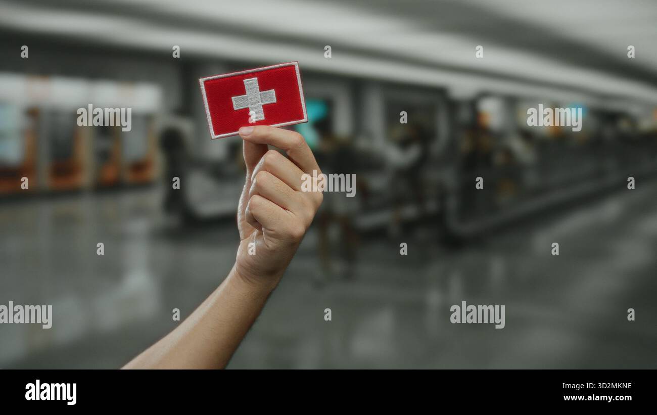 Mann mit schweizer Flaggenstickerei im Innenbereich des Flughafenterminals mit verschwommenem Hintergrund. Stockfoto