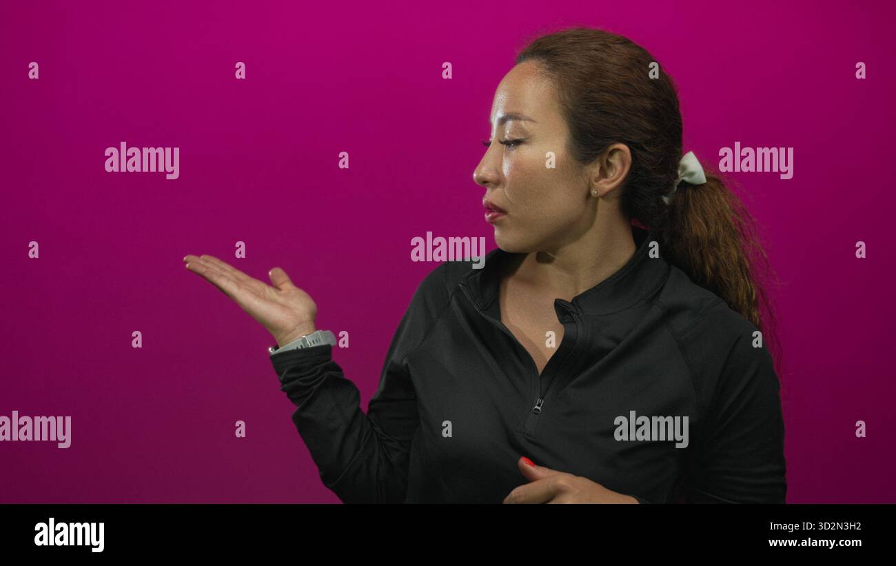 Frau, die im magentafarbenen Atelier einen Reißverschluss an der Brust mit gefesselten Händen schließt, mit neutralem Ausdruck nach vorne gerichtet; Entschlossenheit. Stockfoto