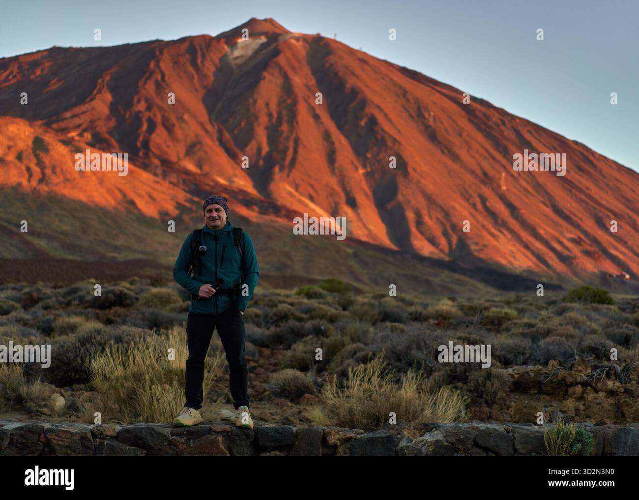 Männlicher Wanderer mit Rucksack und Action-Kamera, der bei Sonnenaufgang vor dem Teide im ersten Licht des morgens steht Stockfoto