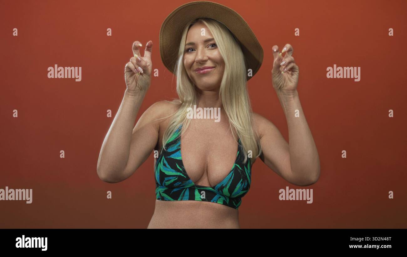 Blonde weiße Frau im Strohhut mit Dekolleté, die im Studio eine Geste zitiert; Sarkasmus Verspieltheit Selbstbewusstsein Humor. Stockfoto