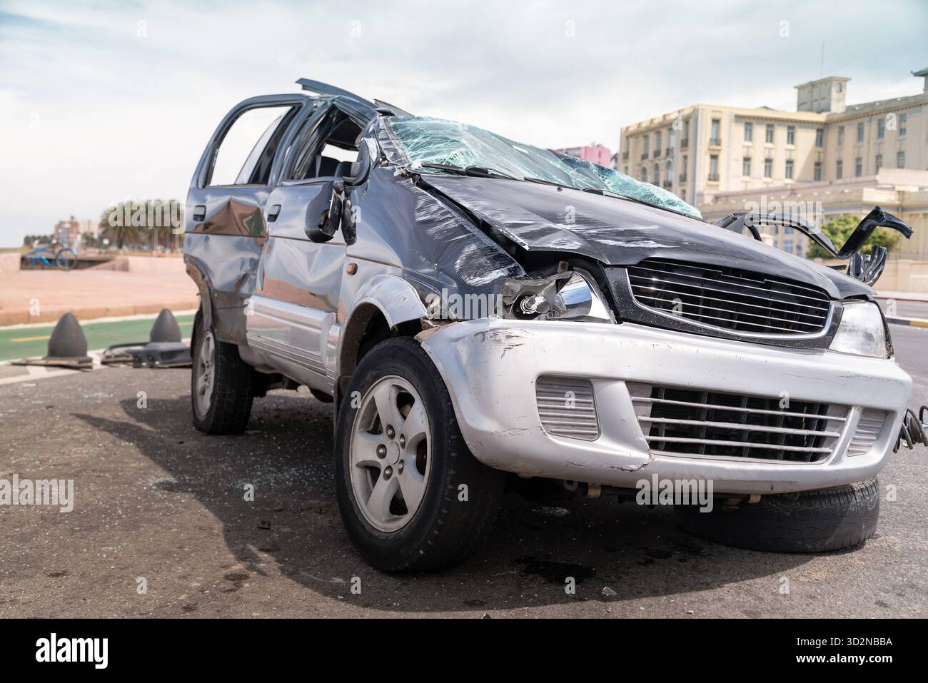Beschädigtes Fahrzeug mit gebrochener Windschutzscheibe und zerknitterter Karosserie, das nach einem Unfall auf einer Straße sitzt Stockfoto