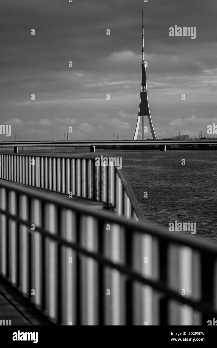 Rigaer Fernsehturm am Daugava Fluss, eingerahmt von goldenen Geländern, die die baltische Architektur, das Wahrzeichen der Stadt und das Symbol der modernen Technik von Latvi veranschaulichen Stockfoto