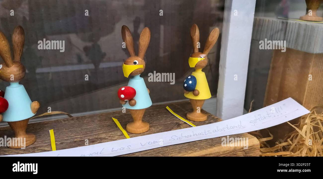Hölzerne Osterhasenfiguren tragen Corona-Schutzmasken, die festliche Dekoration mit Gesundheitsschutzmaßnahmen kombinieren. Stockfoto