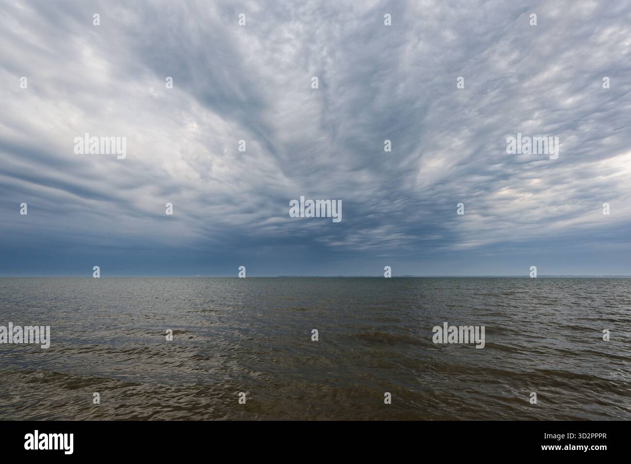 Wellen welken über das Meer, während ein blauer Himmel dünne Wolken zeigt, die wie ein weiches Netz angeordnet sind. Das Licht ist sanft und das Wasser bewegt sich stetig und bildet einen pe Stockfoto