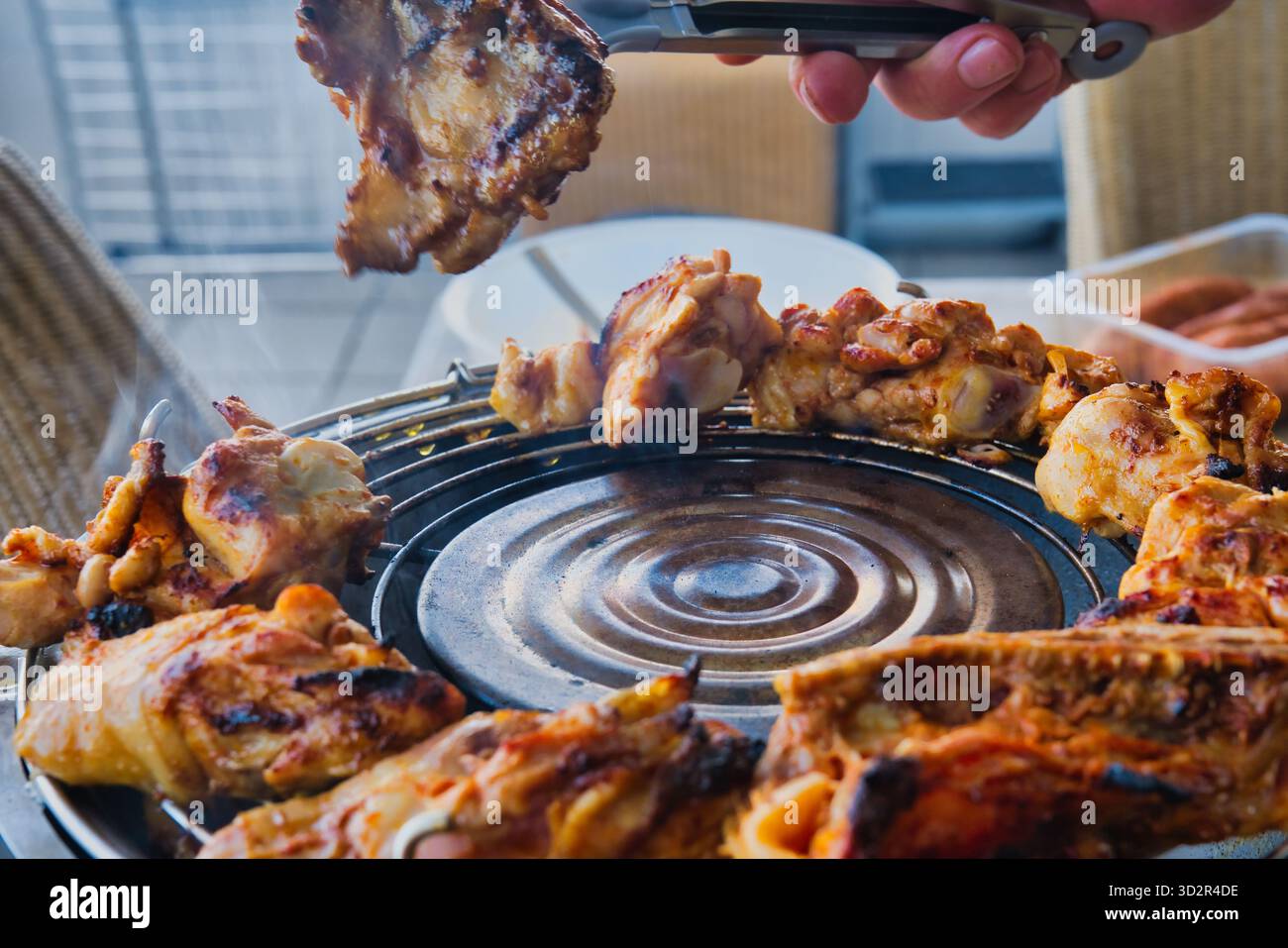 Rauchig gegrilltes Hühnchengrillen auf dem Grill im Freien, saftiges geröstetes Fleisch mit Zange während des Sommerpicknicks, grillzubereitung im Hinterhof Stockfoto