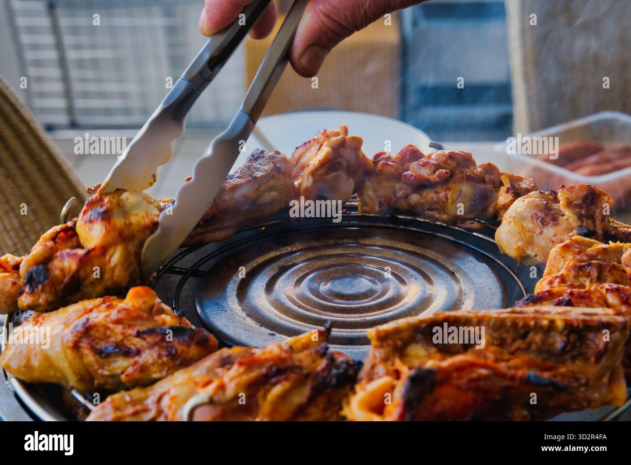 Rauchig gegrilltes Hühnchengrillen auf dem Grill im Freien, saftiges geröstetes Fleisch mit Zange während des Sommerpicknicks, grillzubereitung im Hinterhof Stockfoto