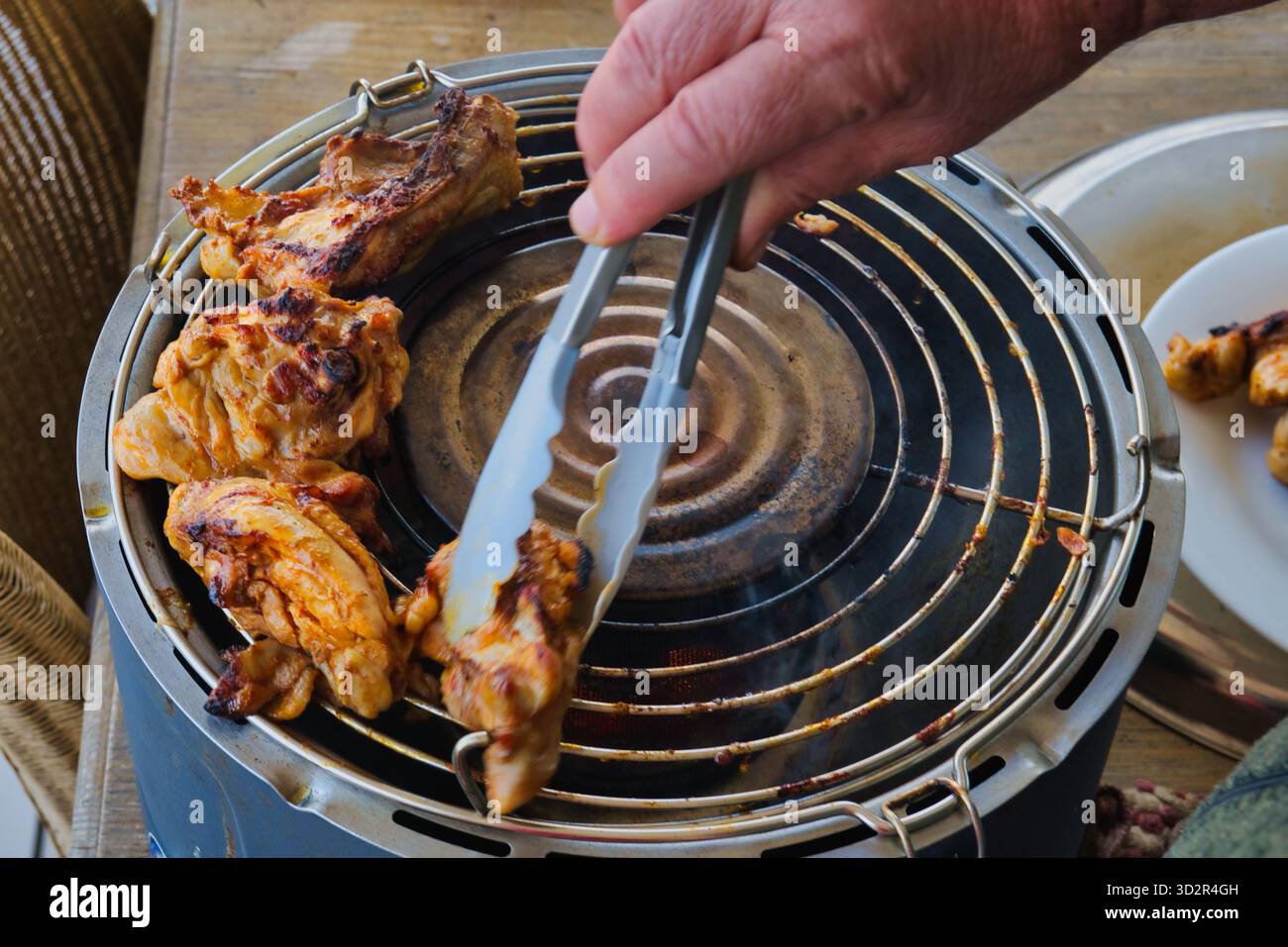 Rauchig gegrilltes Hühnchengrillen auf dem Grill im Freien, saftiges geröstetes Fleisch mit Zange während des Sommerpicknicks, grillzubereitung im Hinterhof Stockfoto