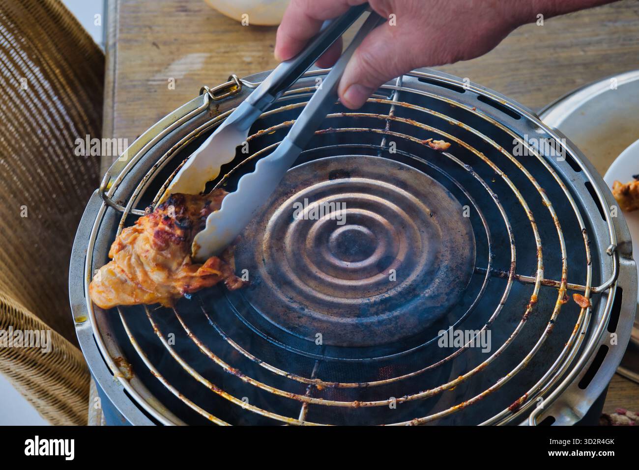 Rauchig gegrilltes Hühnchengrillen auf dem Grill im Freien, saftiges geröstetes Fleisch mit Zange während des Sommerpicknicks, grillzubereitung im Hinterhof Stockfoto